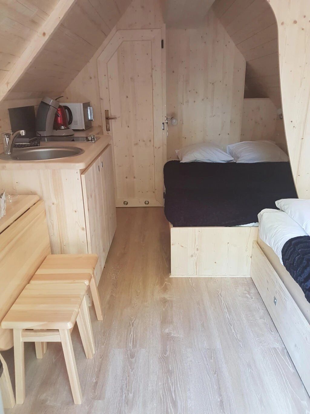Una habitación compacta con kitchenette, cama y una pequeña mesa de madera.