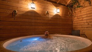 A wooden cabin interior with a hot tub, wooden walls, and hanging lanterns.