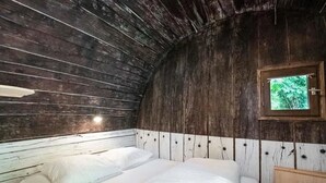 Habitación rústica de cabaña de madera con cama, pequeña ventana con vista a follaje y armario de madera.
