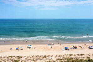 Uma praia com céu claro, mar calmo e pessoas aproveitando a água.