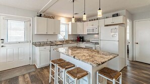 Una cucina moderna con mobili bianchi, un'isola in granito e sgabelli da bar.