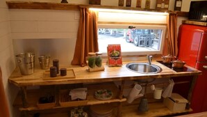 Een kleine keuken met een houten aanrecht, een roestvrijstalen spoelbak en een raam met gordijnen.
