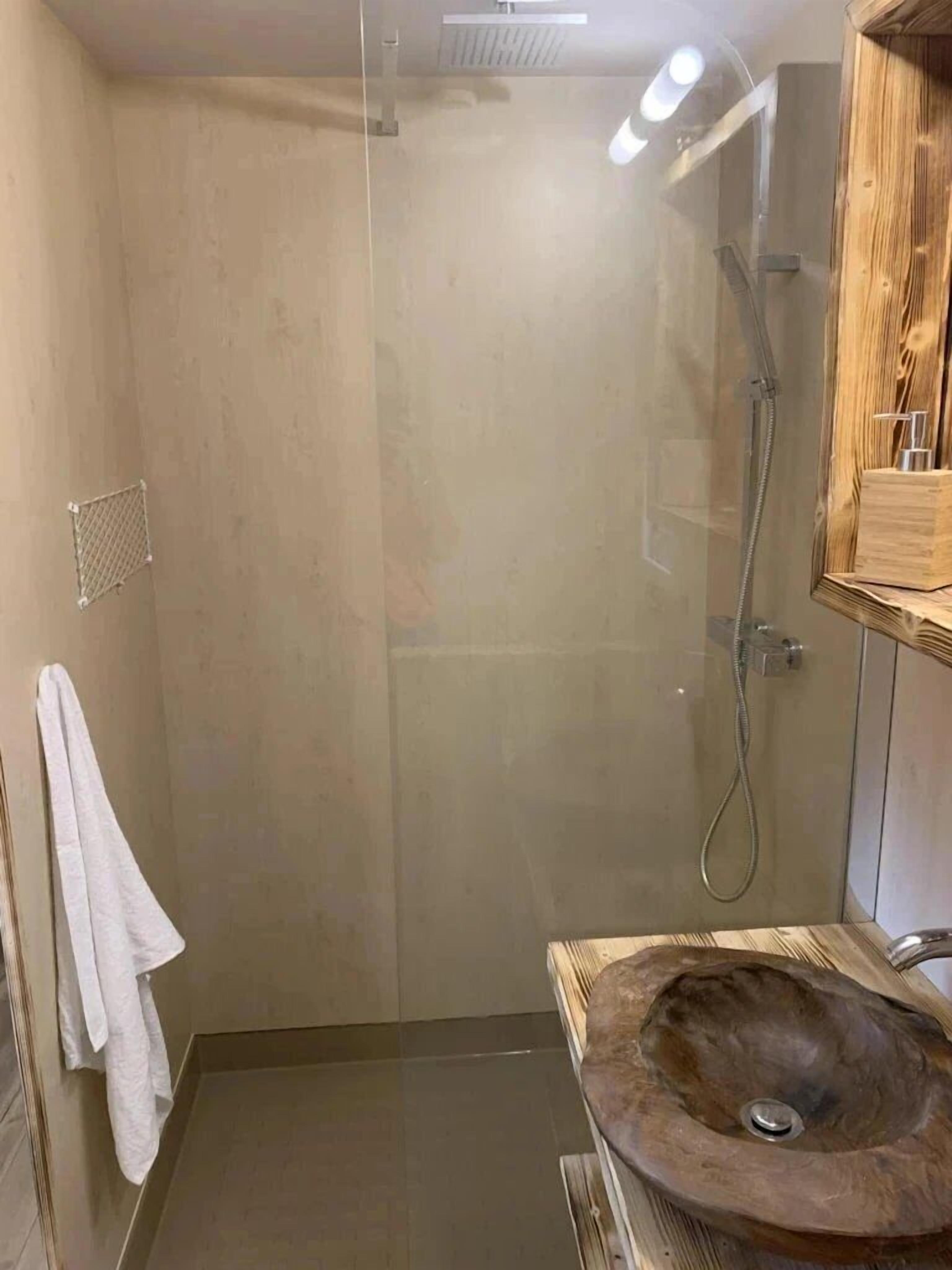 A modern bathroom with a glass-enclosed shower, a wooden vanity with a round sink, and a towel hanging on the wall.