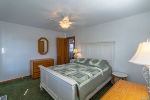 Classic design with a four-poster bed, dresser, and small table, featuring a ceiling fan and window.