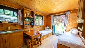A cozy cabin with a wooden interior, a dining area with a table and chairs, a bed with a view, and a kitchen with shelves and a sink. - ZEcamping 2 étoiles piscine couverte dog friendly sauna locatif 18m2 5 pers (Bar-sur-Aube)