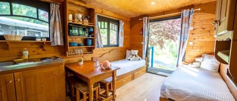 A cozy cabin with a wooden interior, a dining area with a table and chairs, a bed with a view, and a kitchen with shelves and a sink.
