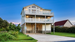A two-story building with a balcony on the upper floor, a covered front porch, and a sign indicating a rental property. - Sun Realty ocean and sound views only 600 ft from semi-private beach access (Nags Head)