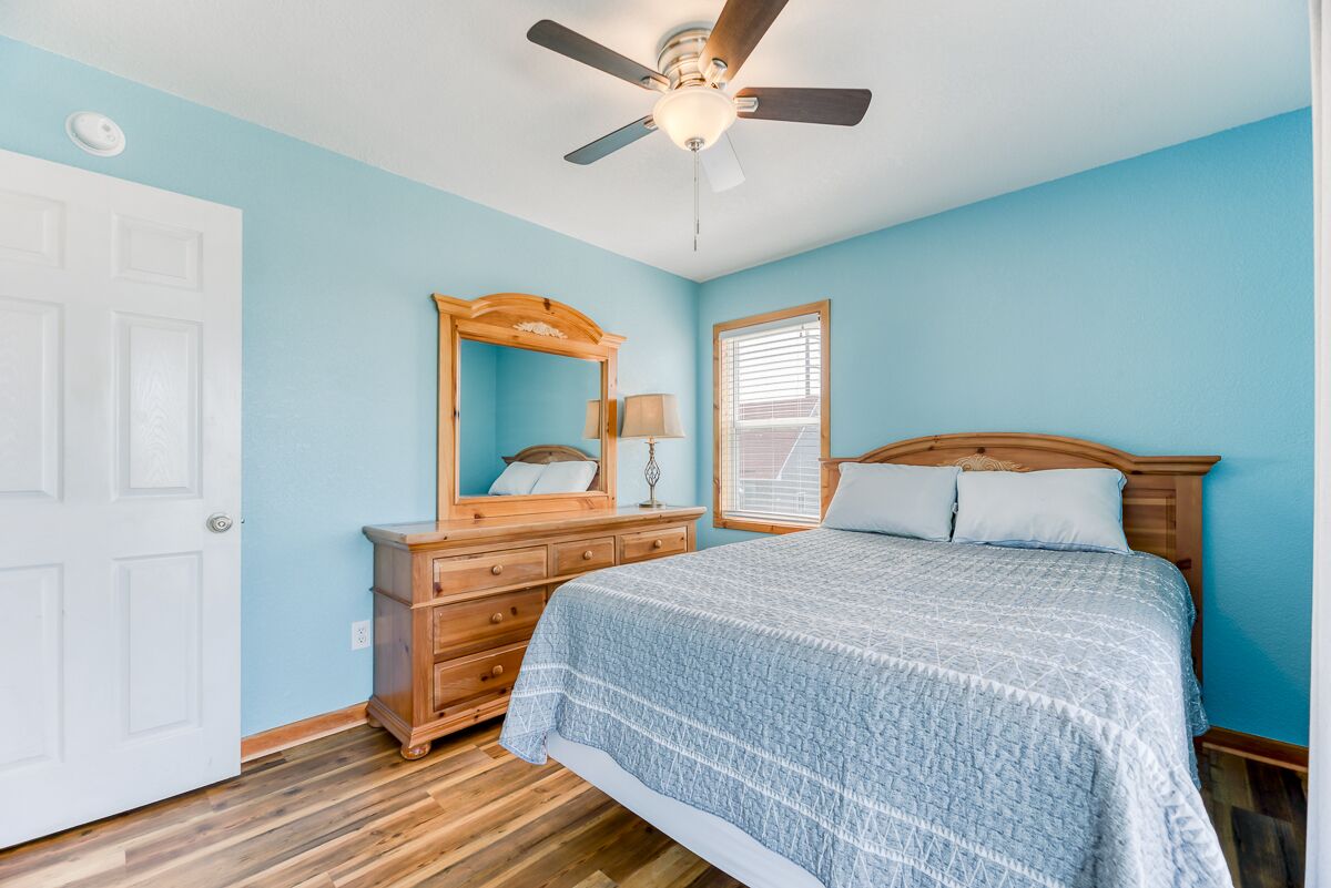 A bedroom with a bed, dresser, mirror, ceiling fan, and window.