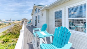 A coastal house with a wooden deck, two turquoise Adirondack chairs, and a view of the beach and other houses. - Sun Realty ocean and sound views only 600 ft from semi-private beach access (Nags Head)