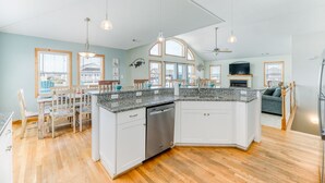 A spacious kitchen with a central island, wooden dining table, and chairs. - Sun Realty ocean and sound views only 600 ft from semi-private beach access (Nags Head)