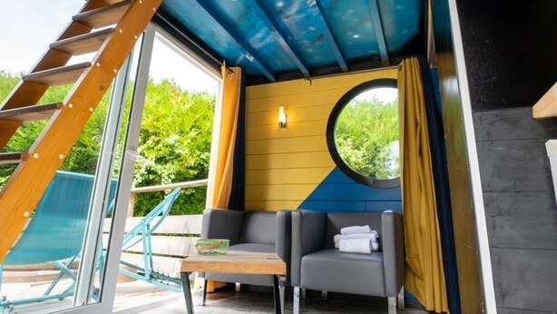A room with a starry ceiling, a round window, a wooden ladder, and a view of greenery outside. - ZEcamping 2 étoiles piscine couverte locatif clim 9m2 (Bar-sur-Aube)