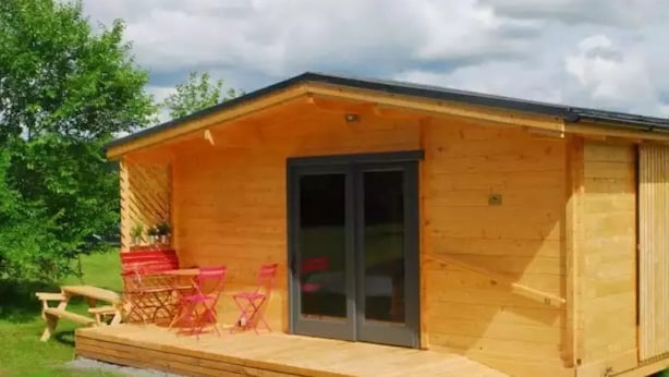 Une cabane en bois dotée d’un patio couvert, d’une porte-fenêtre coulissante et d’une table de pique-nique.