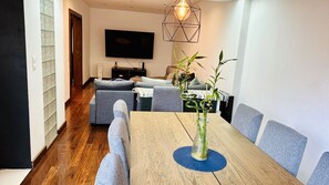 Un soggiorno moderno con un tavolo da pranzo in legno, divani grigi e una TV fissata alla parete.