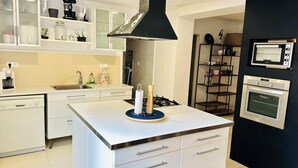 A modern kitchen with white cabinetry, a central island with a gas stove, a black range hood, and built-in ovens.
