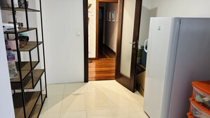 A narrow hallway with a tiled floor, a wooden door, and a white refrigerator on the right.