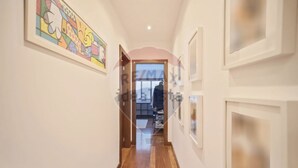 A hallway with wooden flooring, framed artwork on the walls, and a door leading to another room.