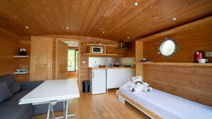 A cozy cabin interior with a kitchenette, a dining area, and a sleeping area with a bed and a teddy bear. - ZEcamping piscine chauffée jacuzzi sauna locatif BBQ clim 25m2 5 pers (Chassenard)