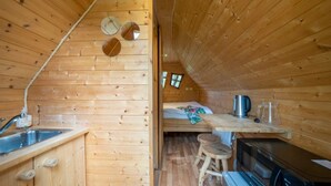 A cozy cabin interior with a wooden interior, a kitchenette with a sink and stove, and a small window. - ZEcamping piscine chauffée animaux acceptés sauna cabane BBQ 6m2 (Chassenard)