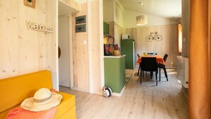 A cozy room with a wooden interior, a dining area with a table and chairs, and a kitchen area with a bicycle mounted on the wall. - ZEcamping 4 étoiles piscine couverte animations chalet TV 35m2 5 pers (Le Bourg-d'Oisans)