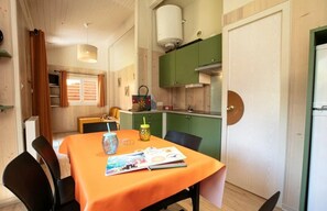 Een kleine keuken met groene kastjes, een witte kookplaat en een eethoek met een oranje tafel.