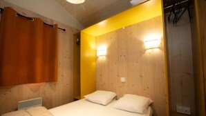 A bedroom with a wooden headboard, two beds with white linens, and a wooden wardrobe with a hanging rack. - ZEcamping 4 étoiles piscine couverte animations chalet TV 35m2 5 pers (Le Bourg-d'Oisans)