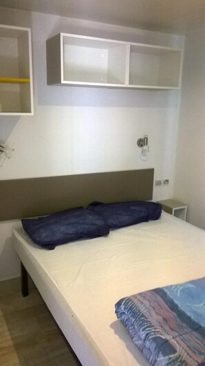 A bedroom with a bed, a headboard, a bedside table, and a shelf above the bed.
