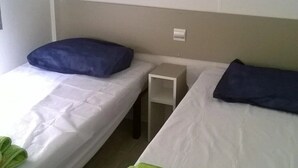 Una habitación con dos camas individuales, cada una con una almohada y una manta verde. Hay dos mesitas de noche blancas entre las camas.