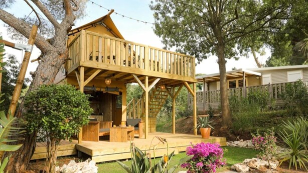 A wooden cabin with a deck, surrounded by a garden with rocks and plants.