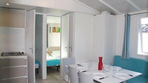 Une pièce compacte comprenant un coin cuisine, une table à manger avec des chaises, un lit et une fenêtre avec des rideaux.