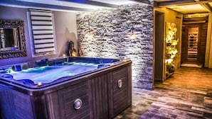 Un espace bien-être comprenant un jacuzzi, un mur en pierre et un plancher en bois.