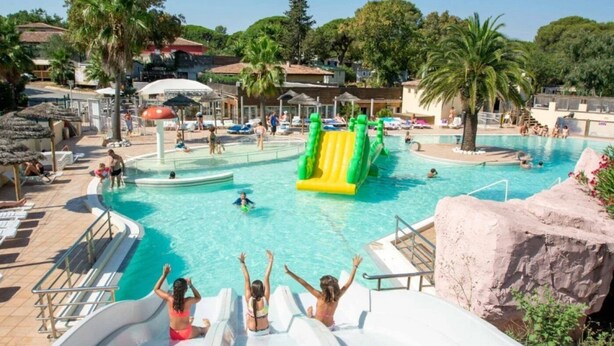 Una piscina con tobogán de agua, sillas de descanso y palmeras.