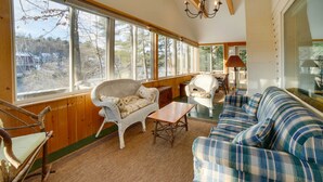 A cozy room with large windows, a wooden floor, a plaid sofa, and a wicker chair. - Lakefront Bradford Cottage w/ Dock, Near Skiing! (Bradford)