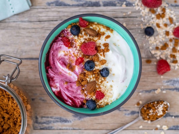 Un bol de yaourt garni de fruits rouges variés et de granola, posé sur une surface en bois.