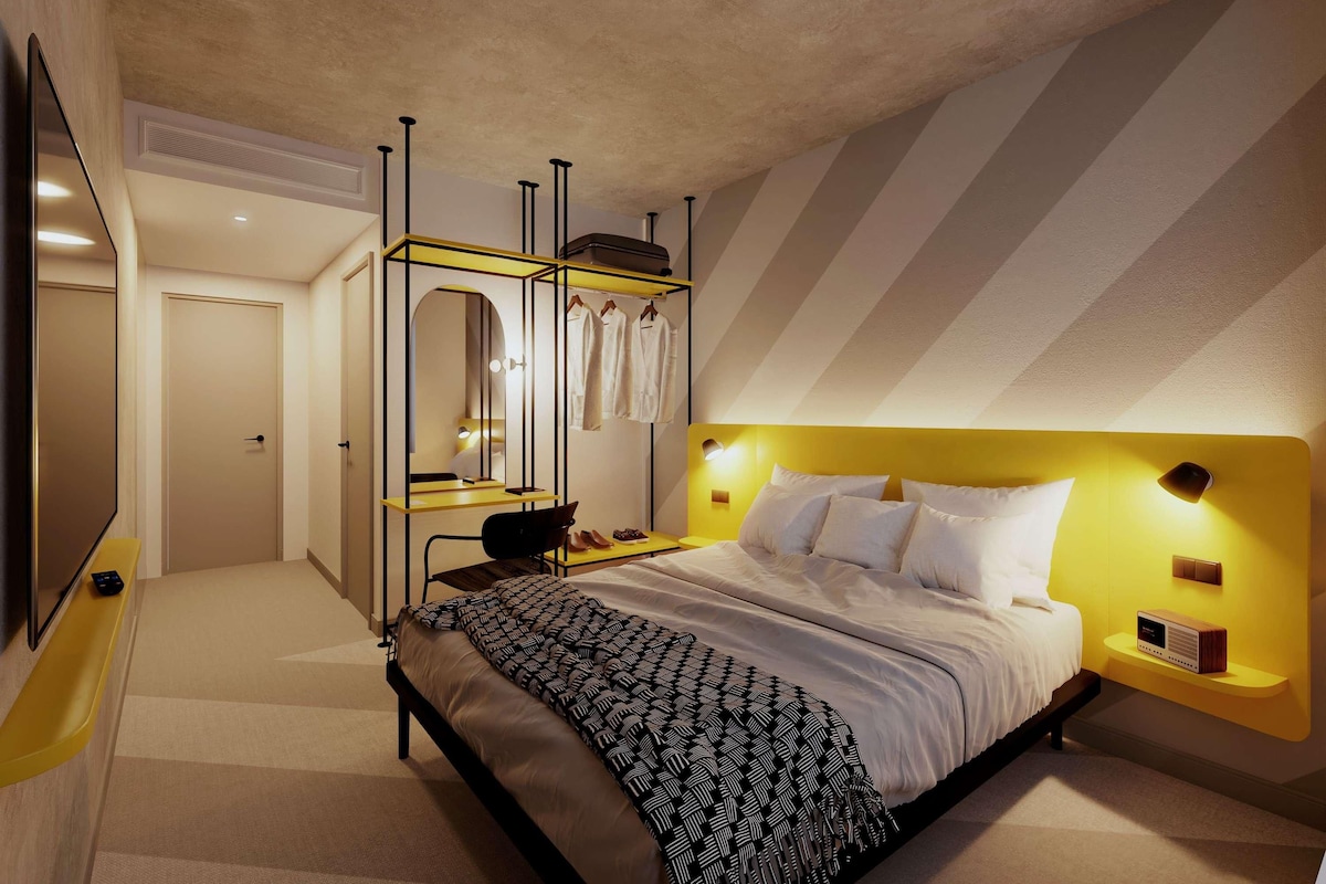 Une chambre à coucher moderne avec un lit, une coiffeuse avec un miroir et un téléviseur.