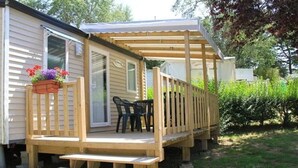 A wooden deck with a bench and chairs, a covered area, and a window with a flower box.