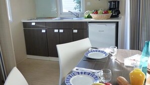 A compact kitchen with a microwave, coffee maker, and a dining table set for two with plates, glasses, and a fruit bowl.