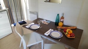 Uma mesa de jantar com pratos, talheres, uma garrafa, um copo, uma baguete e uma travessa de frutas.