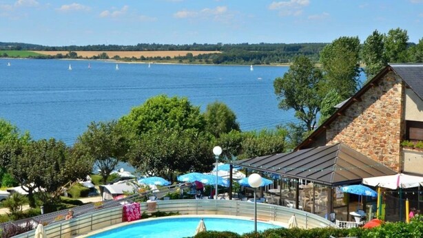Un espace piscine offrant une vue sur un lac et des voiliers, entouré d’arbres et d’un bâtiment en pierre.