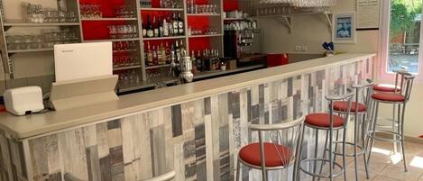 A bar area with stools, shelves stocked with glasses and bottles, and a refrigerator.