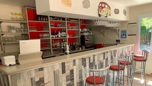 Una zona de bar con taburetes, estantes llenos de vasos y botellas, y un refrigerador.