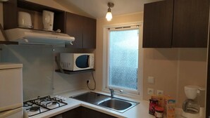 Cocina compacta con estufa a gas, microondas, lavamanos y ventana.