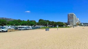 Een strand met campers, een hoog gebouw en bomen op de achtergrond.