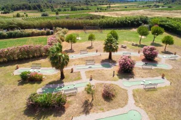 An aerial view of a golf course with multiple greens, trees, and a clear sky.
