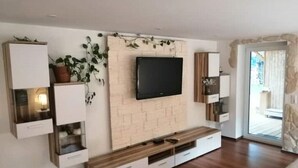 Una sala de estar moderna con un televisor de pantalla plana montado en una pared de ladrillo, armarios de madera y un banco.
