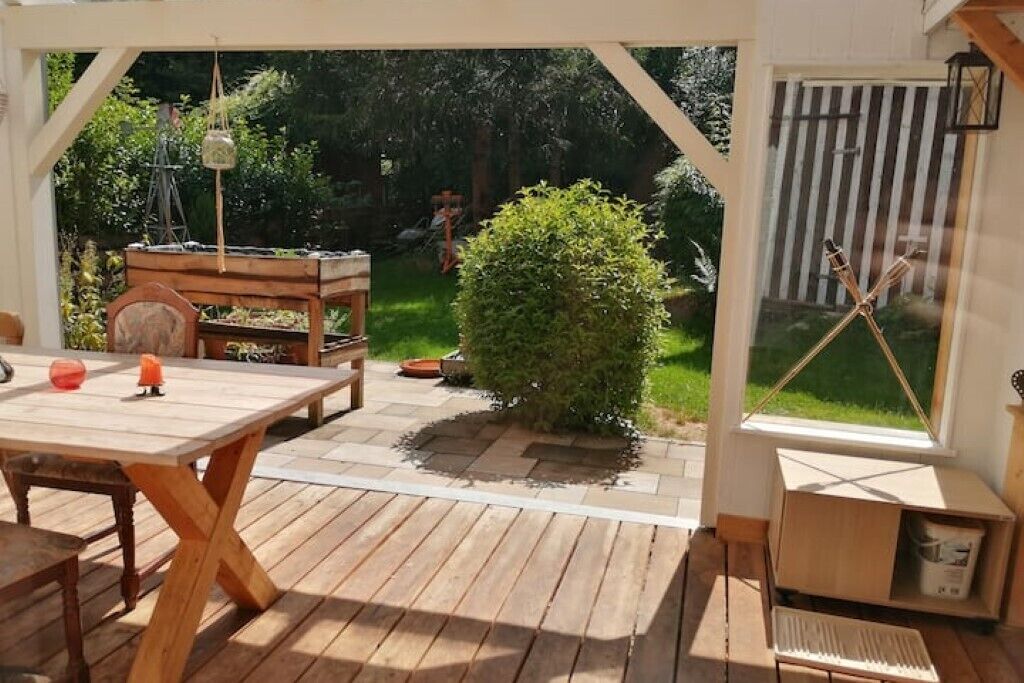 Une terrasse extérieure avec une table et des chaises en bois, un petit banc en bois et une plante en pot.