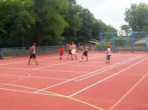 Players enjoy a game of basketball on the outdoor court surrounded by trees.