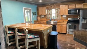 Une cuisine compacte avec des meubles en bois, un îlot central doté de tabourets, un four à micro-ondes, un four traditionnel et un réfrigérateur.