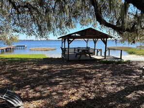 A wooden gazebo with a bench and table, overlooking a lake with a dock. - Lake Clinch Getaway (Frostproof)