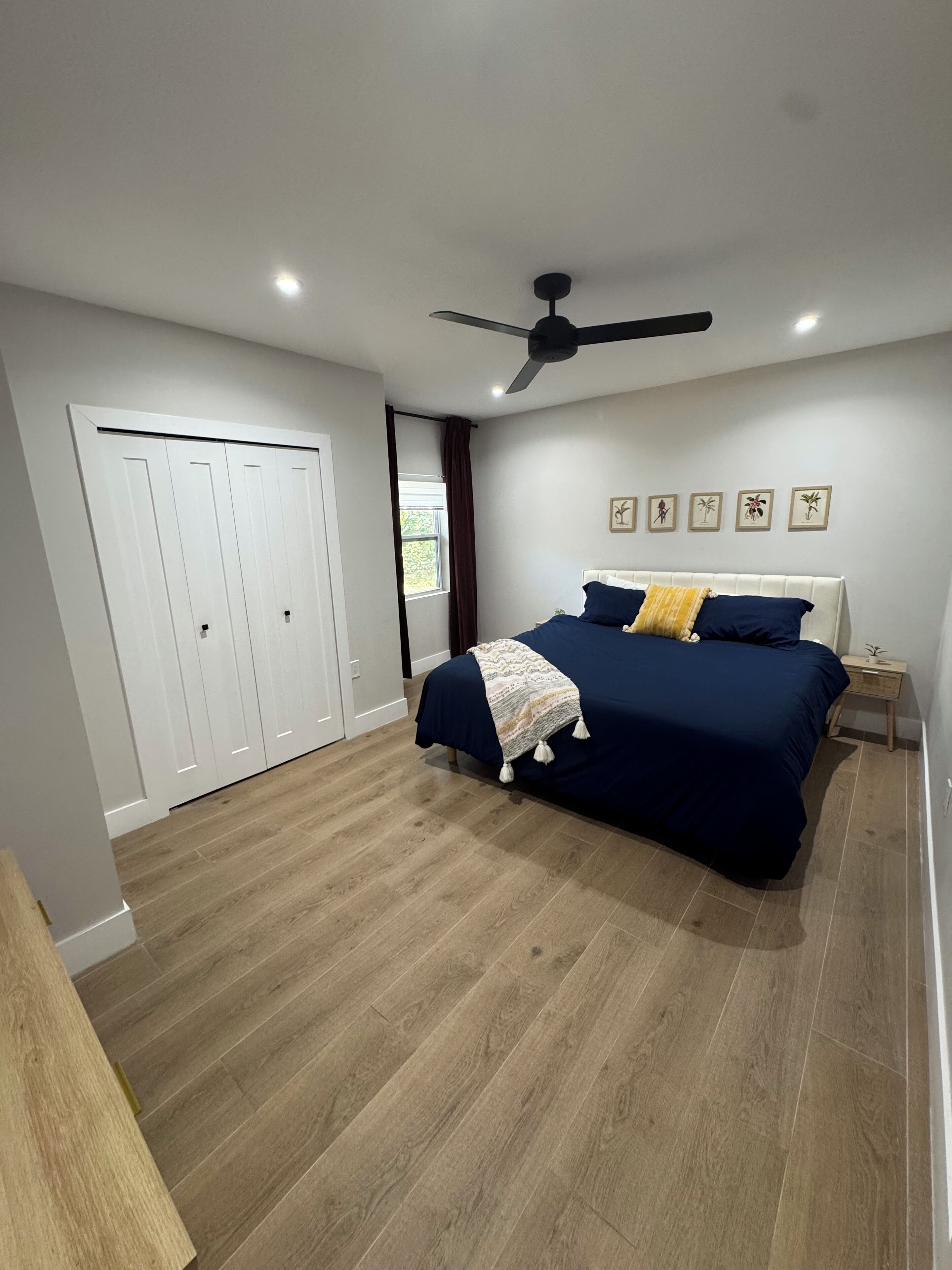 Un dormitorio con cama, ventilador de techo, ventana con cortinas, armario y decoración en la pared.