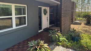 Una casa moderna con fachada gris, una puerta blanca y un pequeño porche con plantas en macetas.